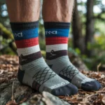 A close-up of a person's feet wearing colorful striped socks while standing on a forest floor covered in leaves and rocks.